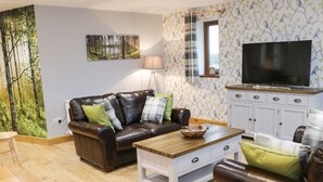 Ein Wohnzimmer mit einem braunen Ledersofa, einem Holztisch und einem Fernseher auf einem Schrank.