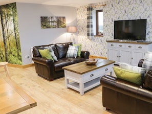A living room with a brown leather sofa, a wooden coffee table, and a television on a cabinet. - Woodman's Lodge (Nantwich)