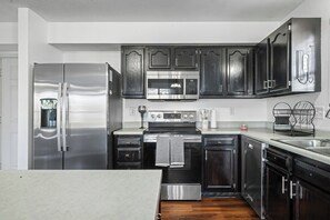 A modern kitchen with stainless steel appliances, dark cabinetry, and a white countertop. - Roadmap Lodging: 3BR Near Mill Race Park, Monthly (Columbus)