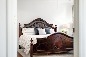 A bedroom with a wooden bed, white walls, and a nightstand with a lamp. - Roadmap Lodging: 3BR Near Mill Race Park, Monthly (Columbus)