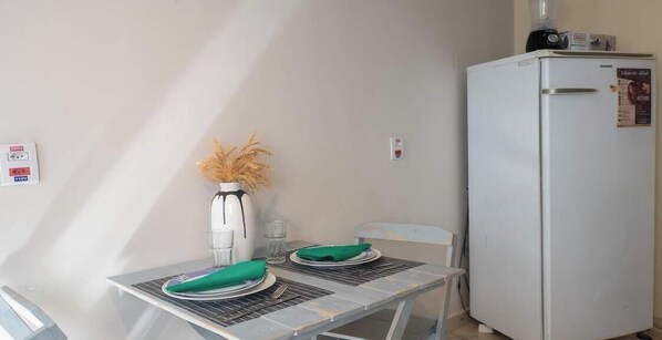 A dining table with two plates, a vase with dried flowers, and a white refrigerator.