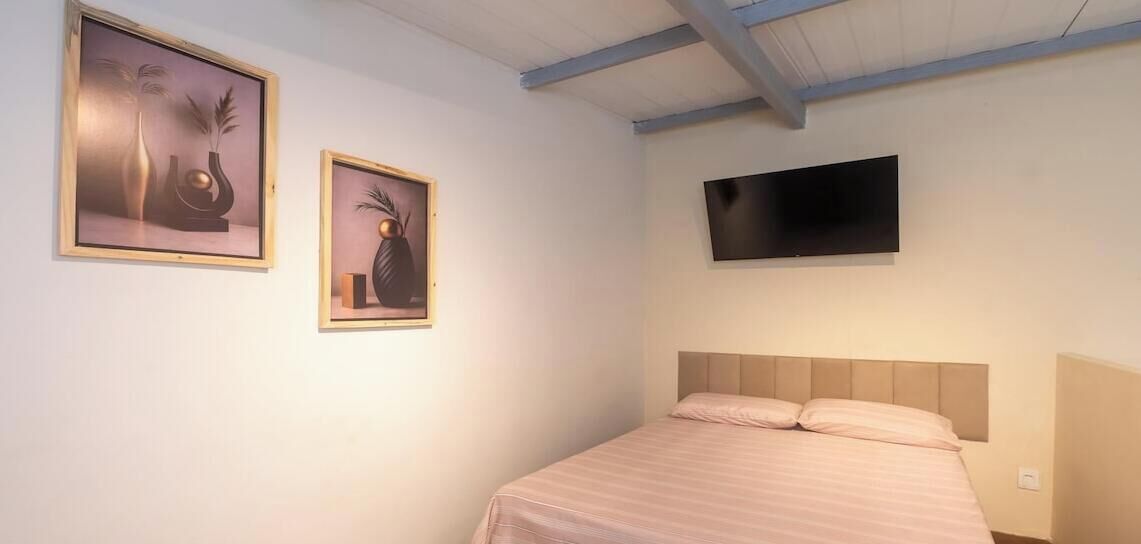A bedroom with a bed, a television mounted on the wall, and two framed artworks on the wall.