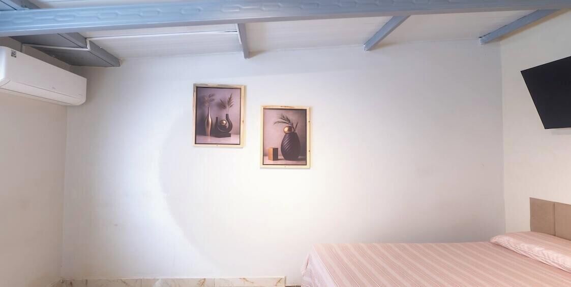 Ein Schlafzimmer mit einem Bett, einem an der Wand befestigten Fernseher und zwei gerahmten Bildern.