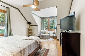 A bedroom with a bed, a television, a ceiling fan, a window, and a chair.