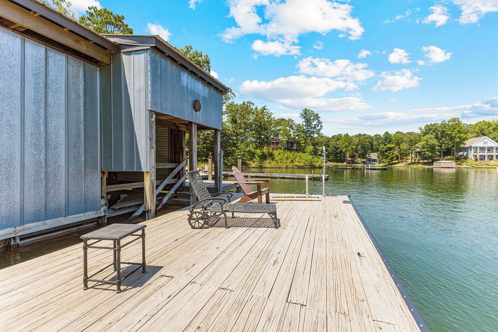 A wooden dock extending into a calm lake, with a metal structure on the left and a clear sky above.