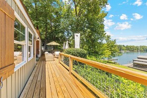 A wooden deck with outdoor furniture, a view of a lake, and a fenced area with greenery. - New! 2 home property on Lake Martin, sleeps 12! (Dadeville)