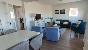 A modern living room with a dining area, a flat-screen TV, and a sofa set. - Apartment 'ViewRoyal' with Sea View, Balcony and Wi-Fi (Katwijk)