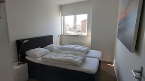 A bedroom with a bed, a bedside table, a lamp, a window, and a radiator. - Apartment 'ViewRoyal' with Sea View, Balcony and Wi-Fi (Katwijk)