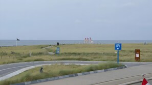 Eine Küstenstraße mit Parkschild, Fußweg und Strand im Hintergrund.