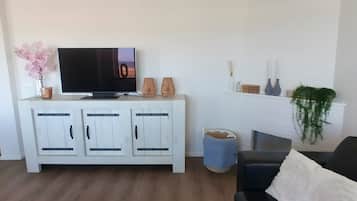 Ein Wohnzimmer mit Flachbildfernseher, weißen Schränken, einem blauen Hocker, einer schwarzen Couch und einem weißen Kaminvorsatz mit Dekoration.