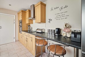 A modern kitchen with wooden cabinets, stainless steel appliances, and a bar stool. - Host Stay Norwood Street (Scarborough)