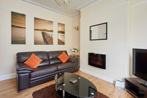 A living room with a leather sofa, a glass coffee table, a flat-screen TV, and artwork on the wall. - Host Stay Norwood Street (Scarborough)