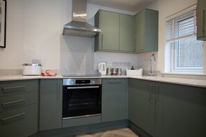 A kitchen with a built-in oven, a coffee maker, and a window with blinds. - Pinot Perch - With Free Underground Parking (Whitby)