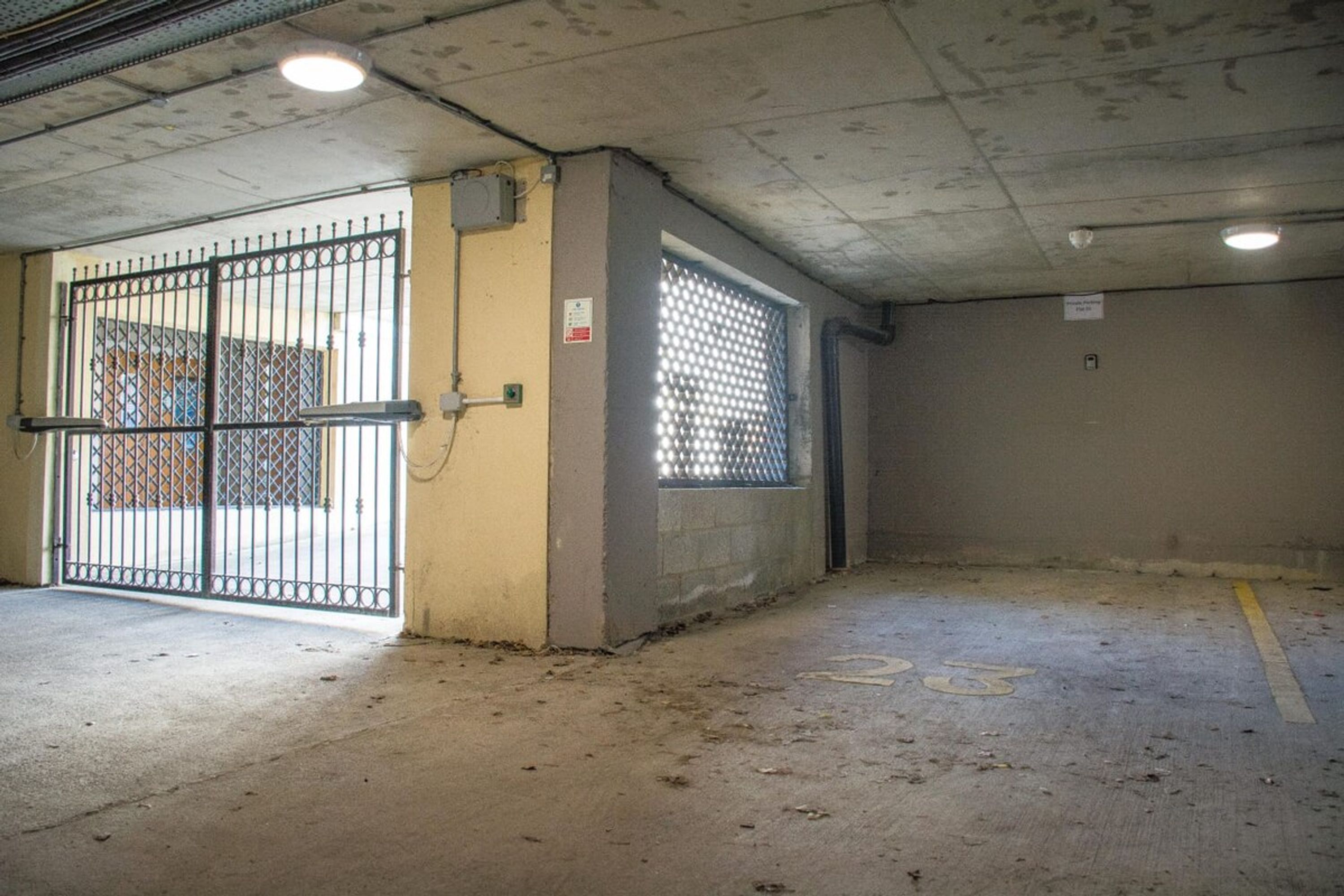 A parking garage with a gated entrance, concrete walls, and a floor marked with parking spaces.