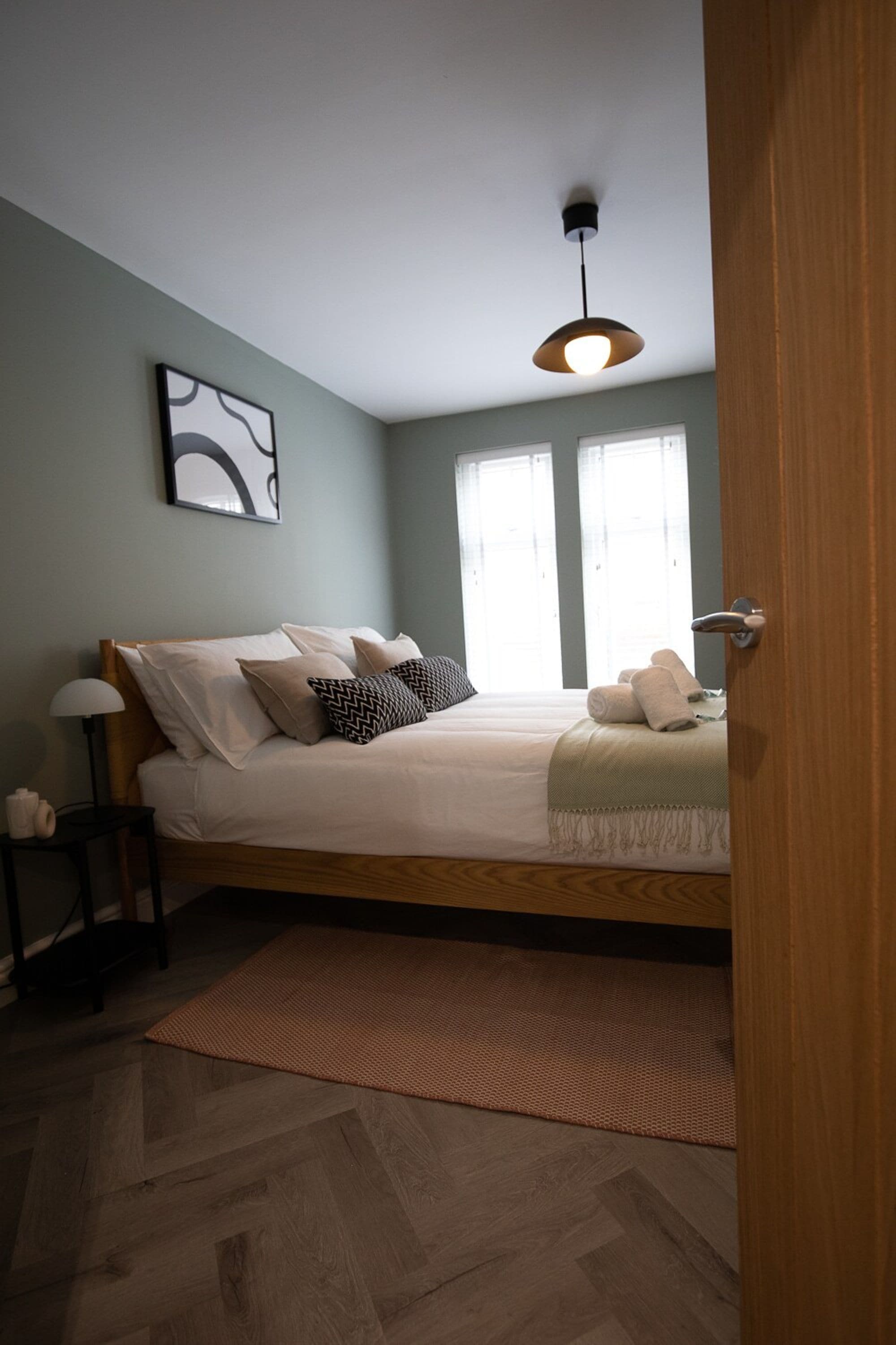 A bedroom with a bed, a bedside lamp, a rug, and a window.