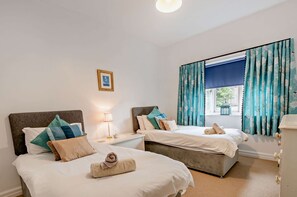Habitación de hotel con dos camas, una mesita de noche con lámpara, un cuadro en la pared y una ventana con cortinas.