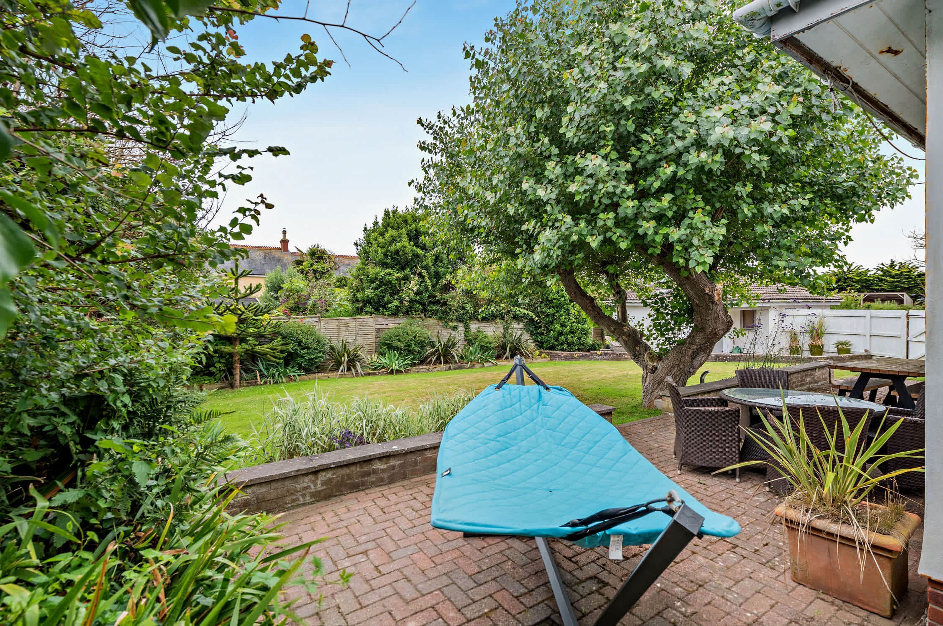 A patio with a blue awning, a brick pathway, and a garden with various plants and a tree.