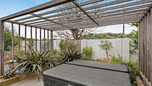 Uma banheira de hidromassagem sob uma pérgola de madeira, com vista para o jardim.