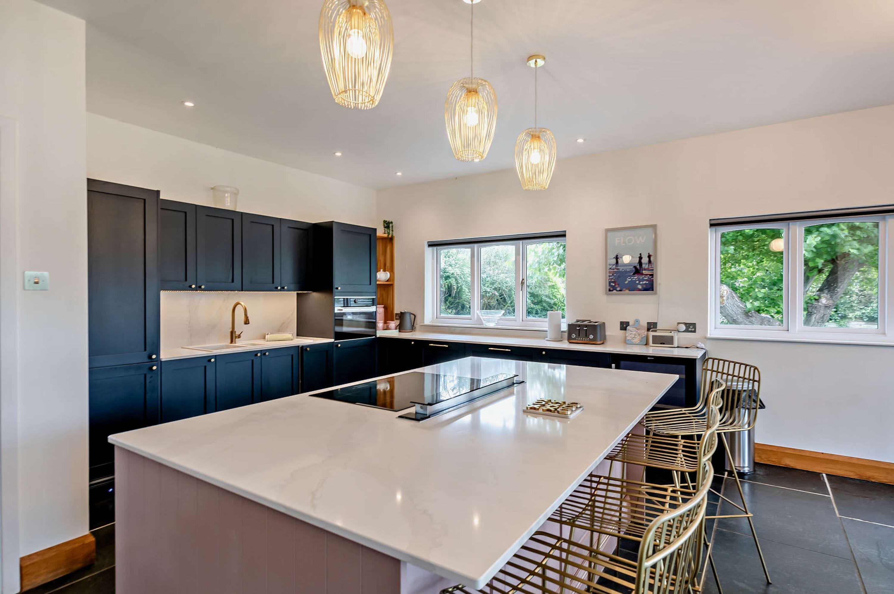 A modern kitchen with dark cabinets, a large island, and pendant lighting.