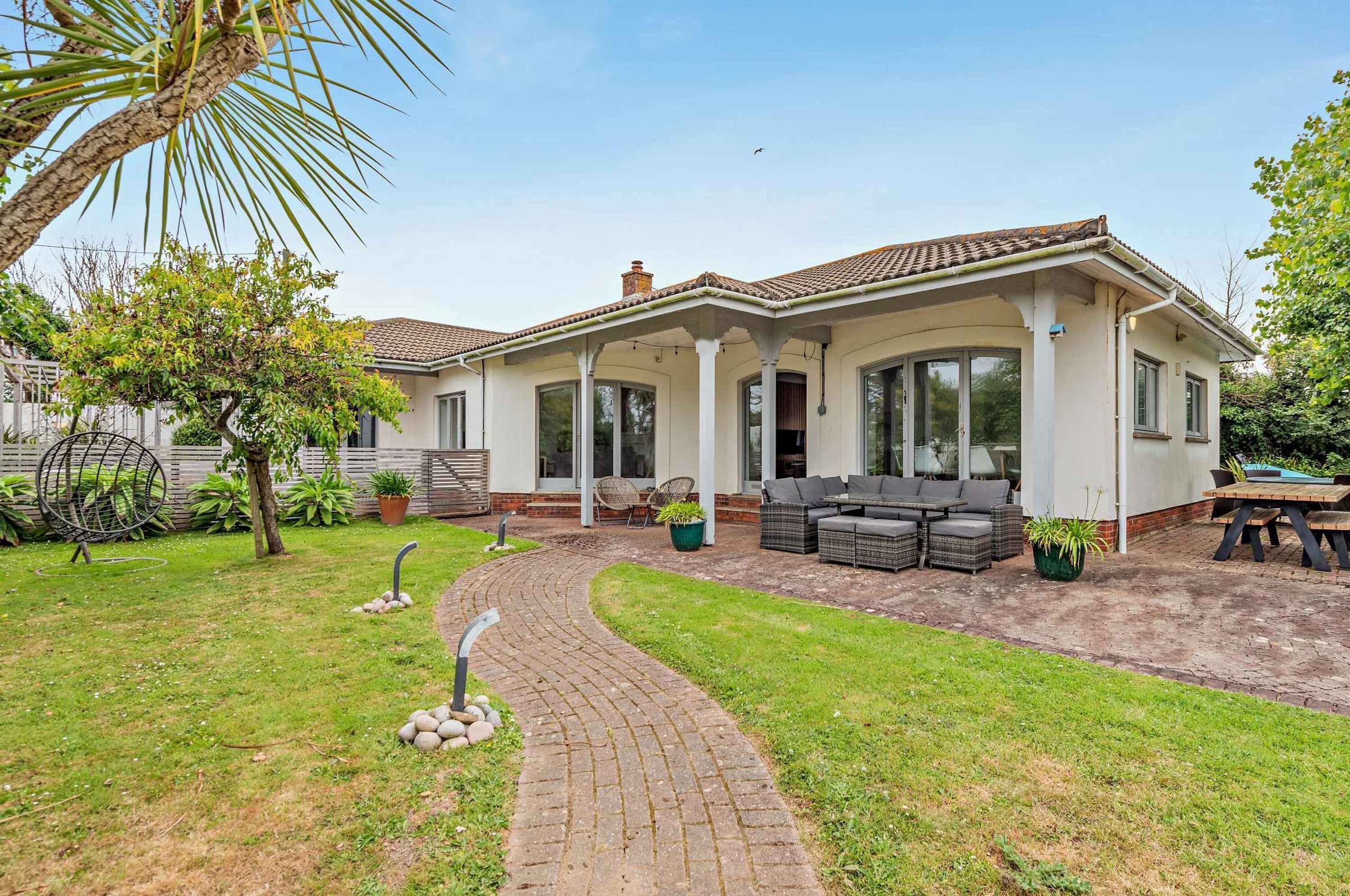 A two-story house with a covered patio, outdoor seating, and a paved pathway.