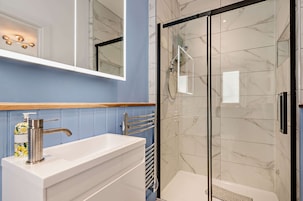 A modern bathroom with a glass shower enclosure, a white vanity with a single faucet, and a blue tiled wall.
