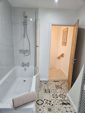 Un bagno con vasca, doccia e una porta che dà su un'altra stanza.