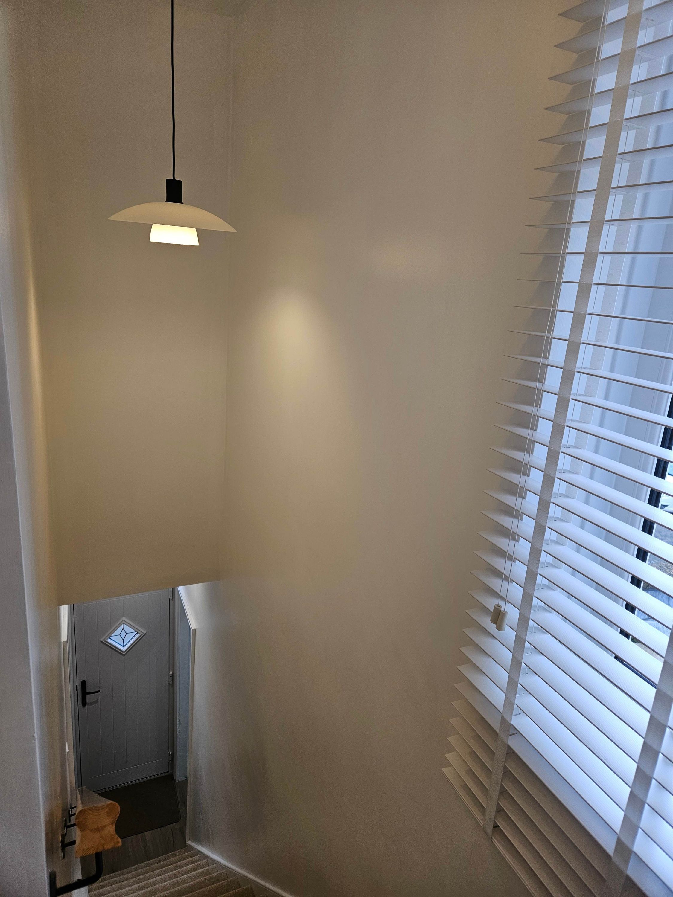 A room with a door leading to a staircase, a hanging light fixture, and a window with blinds.