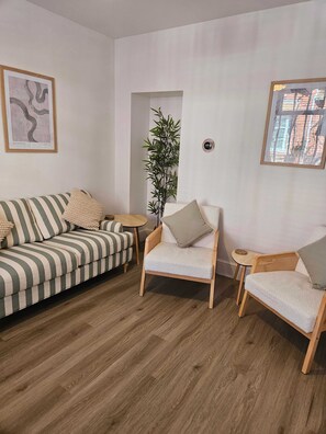 Ein Zimmer mit einem gestreiften Sofa, zwei Sesseln, einem kleinen Tisch, einer Topfpflanze und gerahmten Kunstwerken an den Wänden.