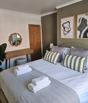 Una camera d'albergo con un letto grande, una scrivania, uno specchio e due quadri astratti appesi al muro.