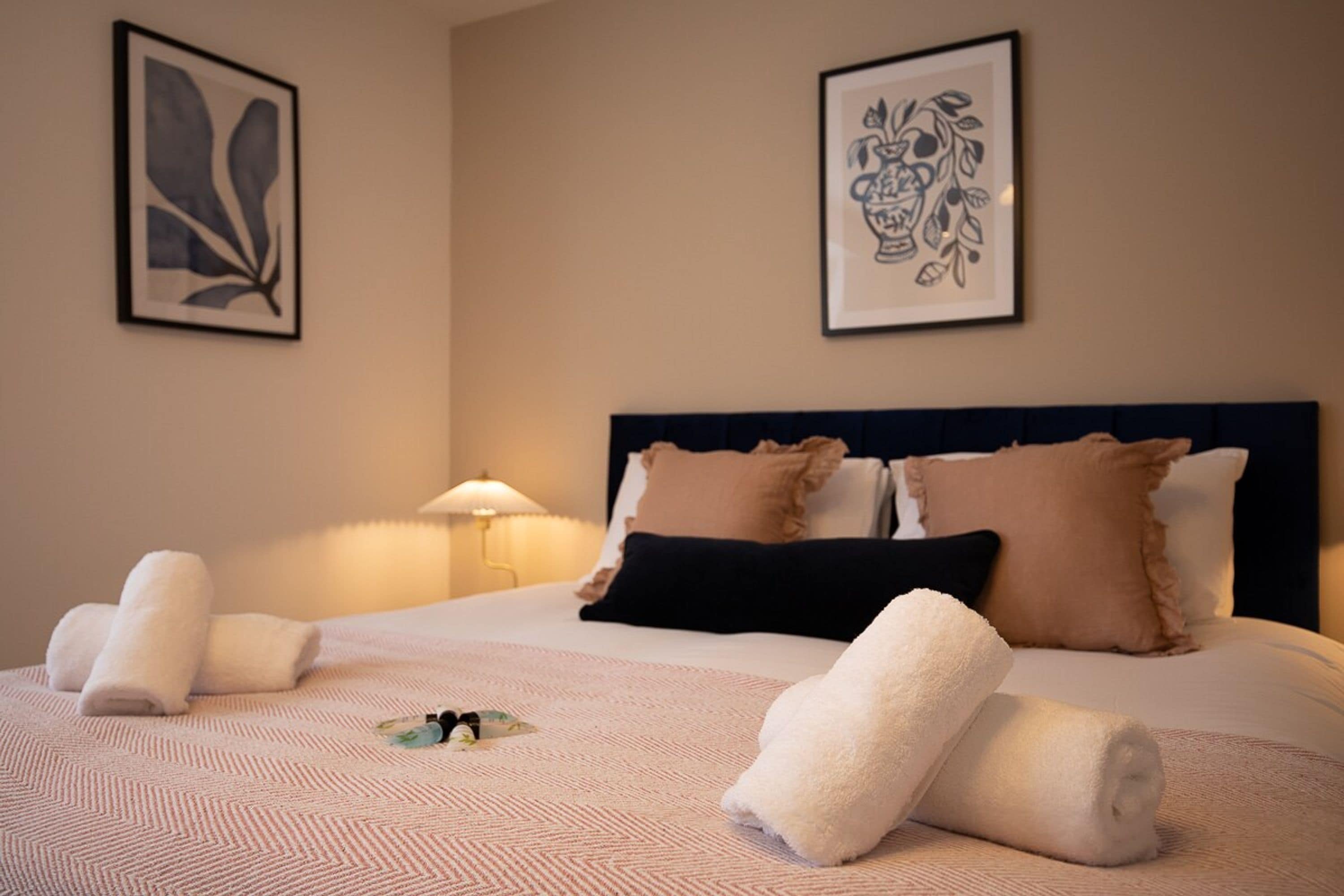 A hotel room with a bed, pillows, a lamp, and artwork on the walls.