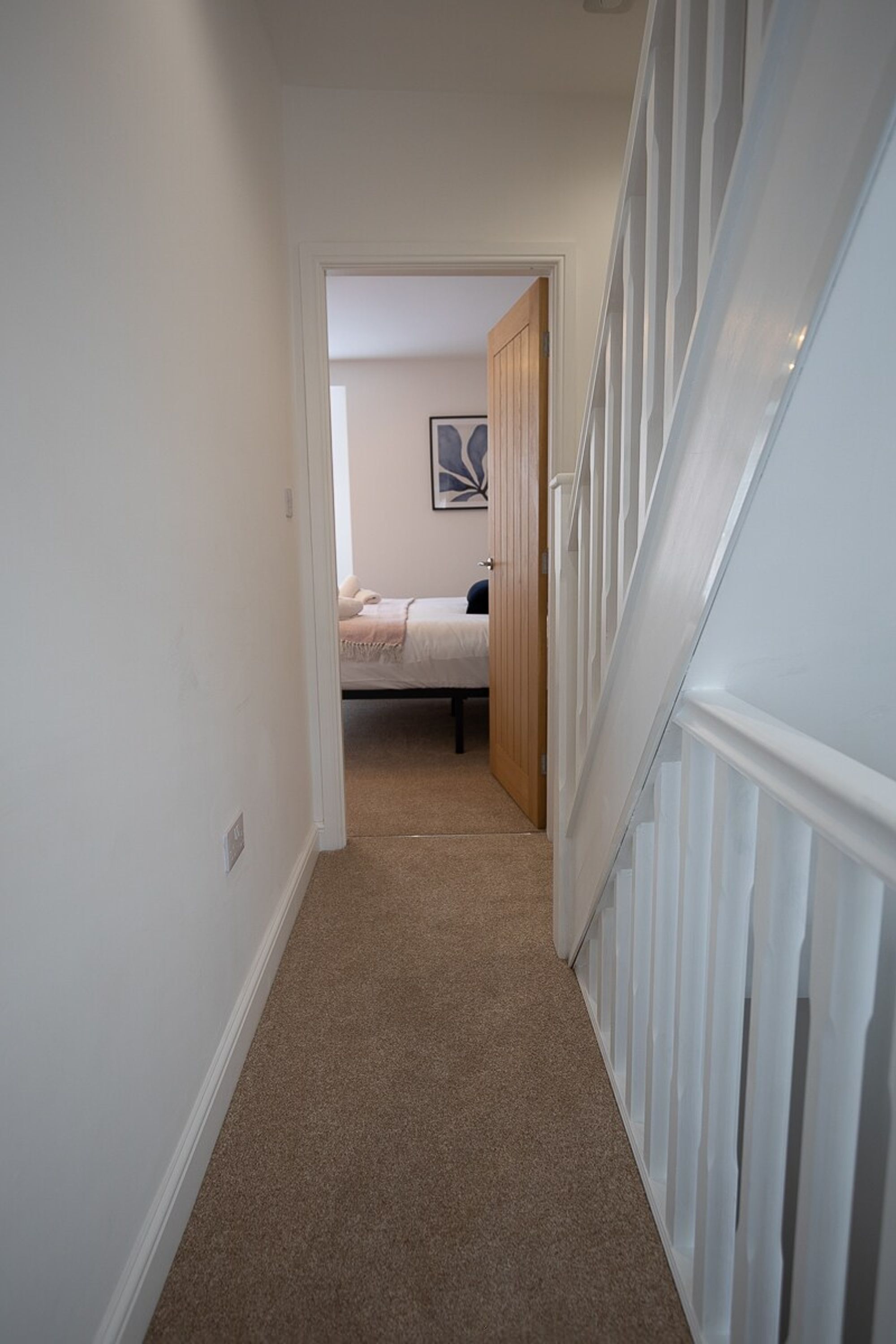 Ein Flur, der zu einem Schlafzimmer mit Bett, Tür und Treppe führt.