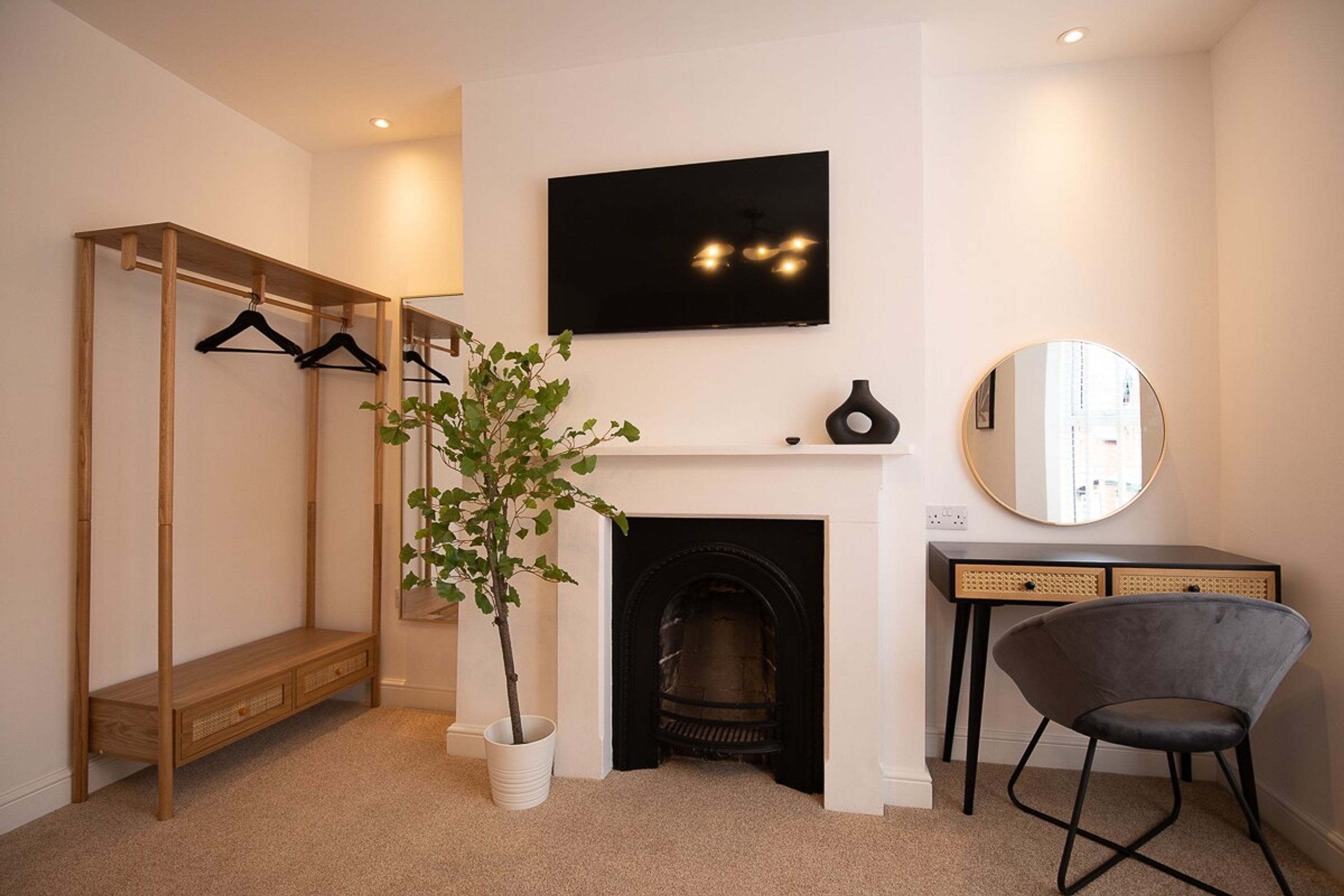 A modern room with a wooden coat rack, a potted plant, a fireplace, a mirror, and a chair.