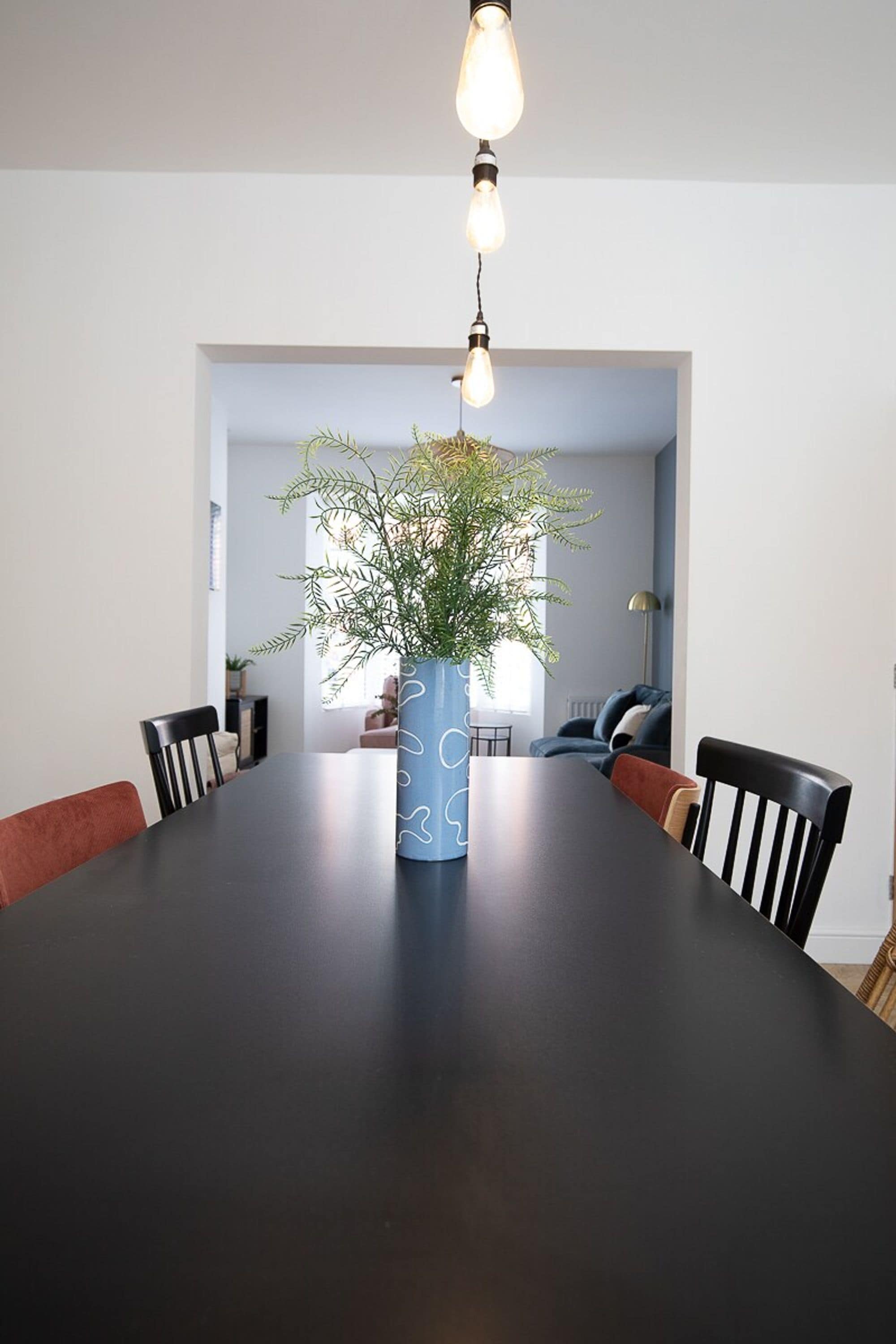 A dining table with chairs, a vase with a plant, and a hanging light fixture.