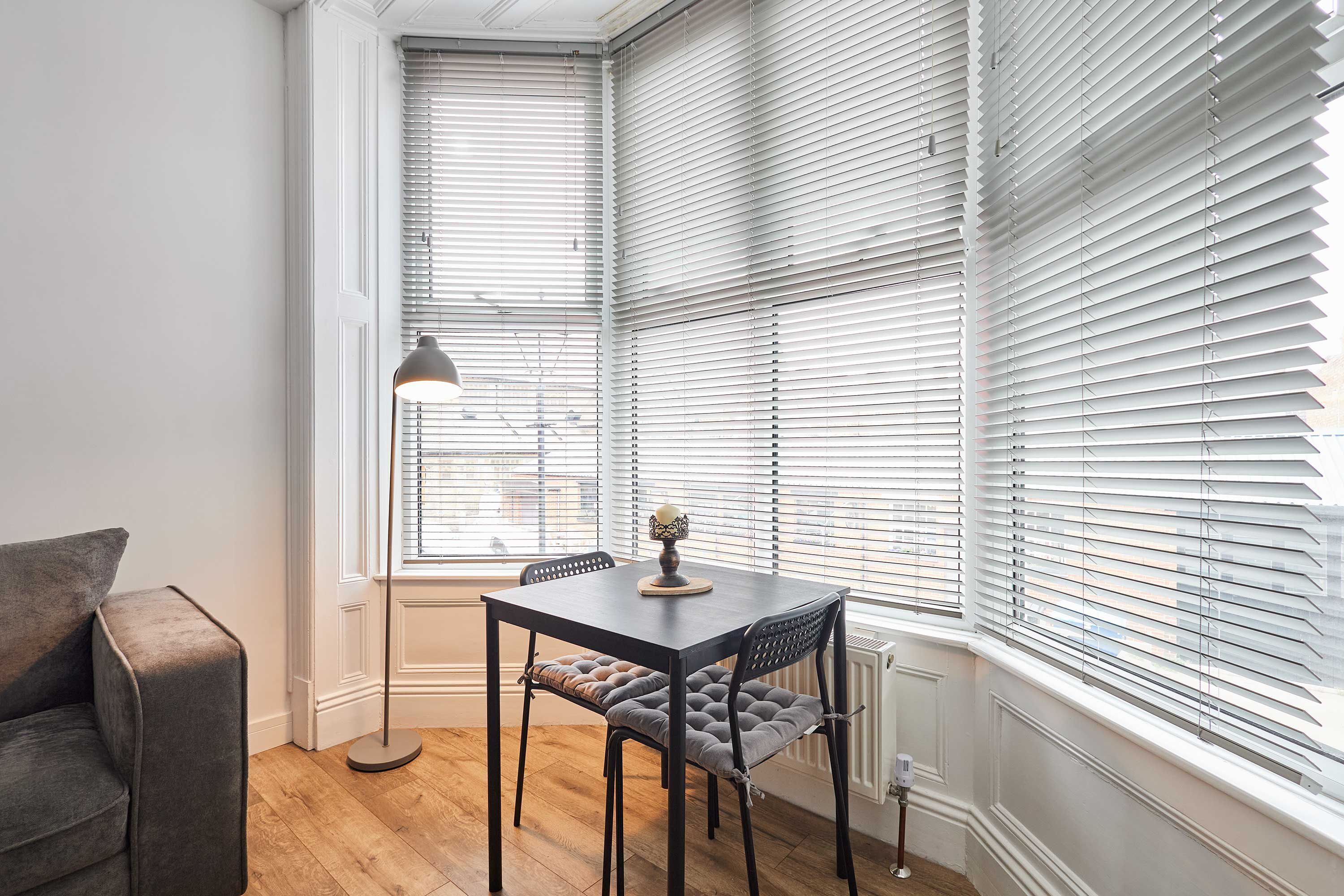Une pièce comprenant une table à manger, deux chaises, un lampadaire et un radiateur.