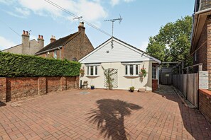 A residential property with a paved driveway, a white house with a pitched roof, and a brick wall with a metal gate. - Host Stay Thornbank (Chichester)
