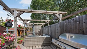 En træterrasse med grill, pergola og blomster i krukker.