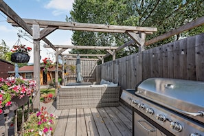 En träaltan med en grill, en pergola och blommor i krukor.