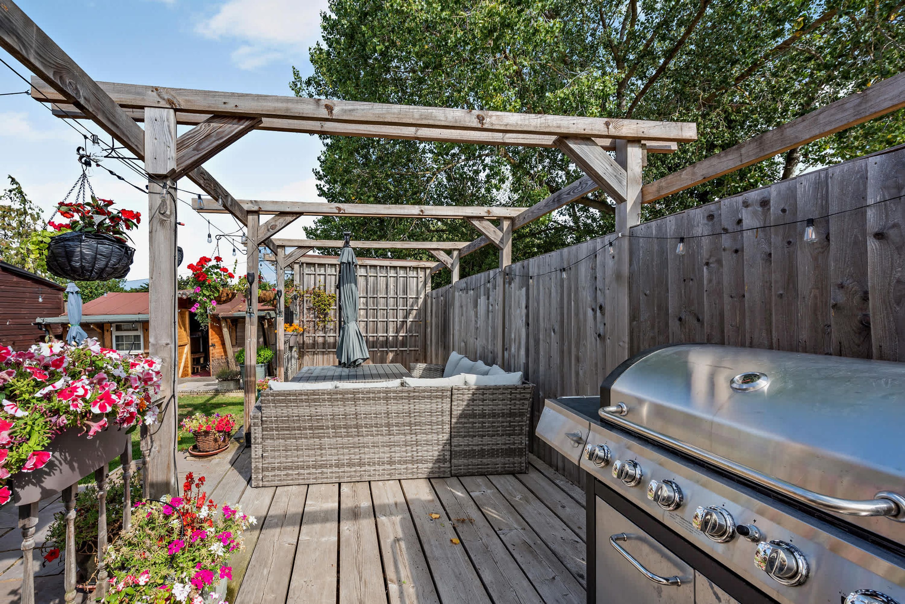 A wooden deck with a barbecue grill, a pergola, and potted flowers.