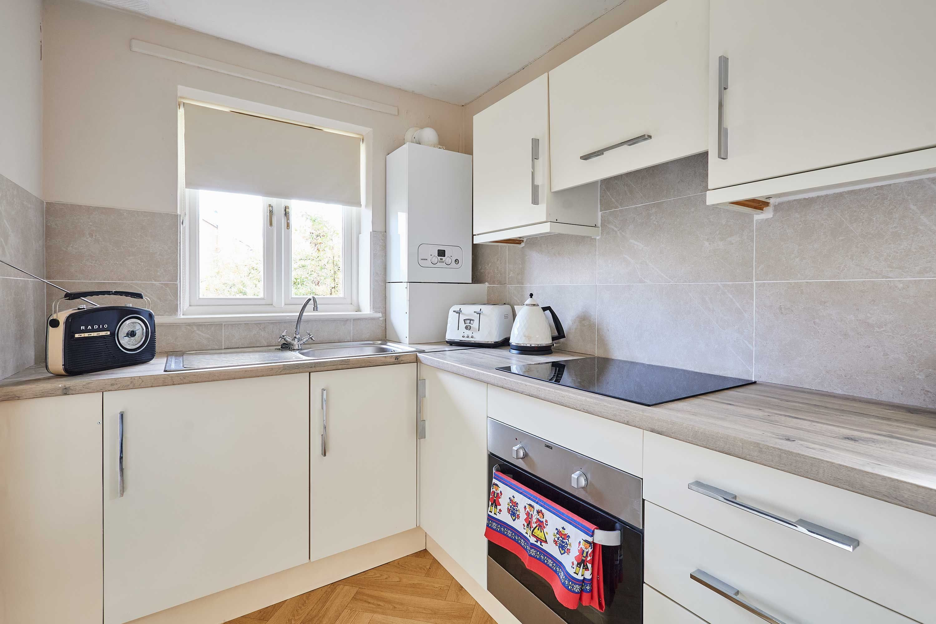 A modern kitchen with white cabinets, a built-in oven, a microwave, and a window above the sink.