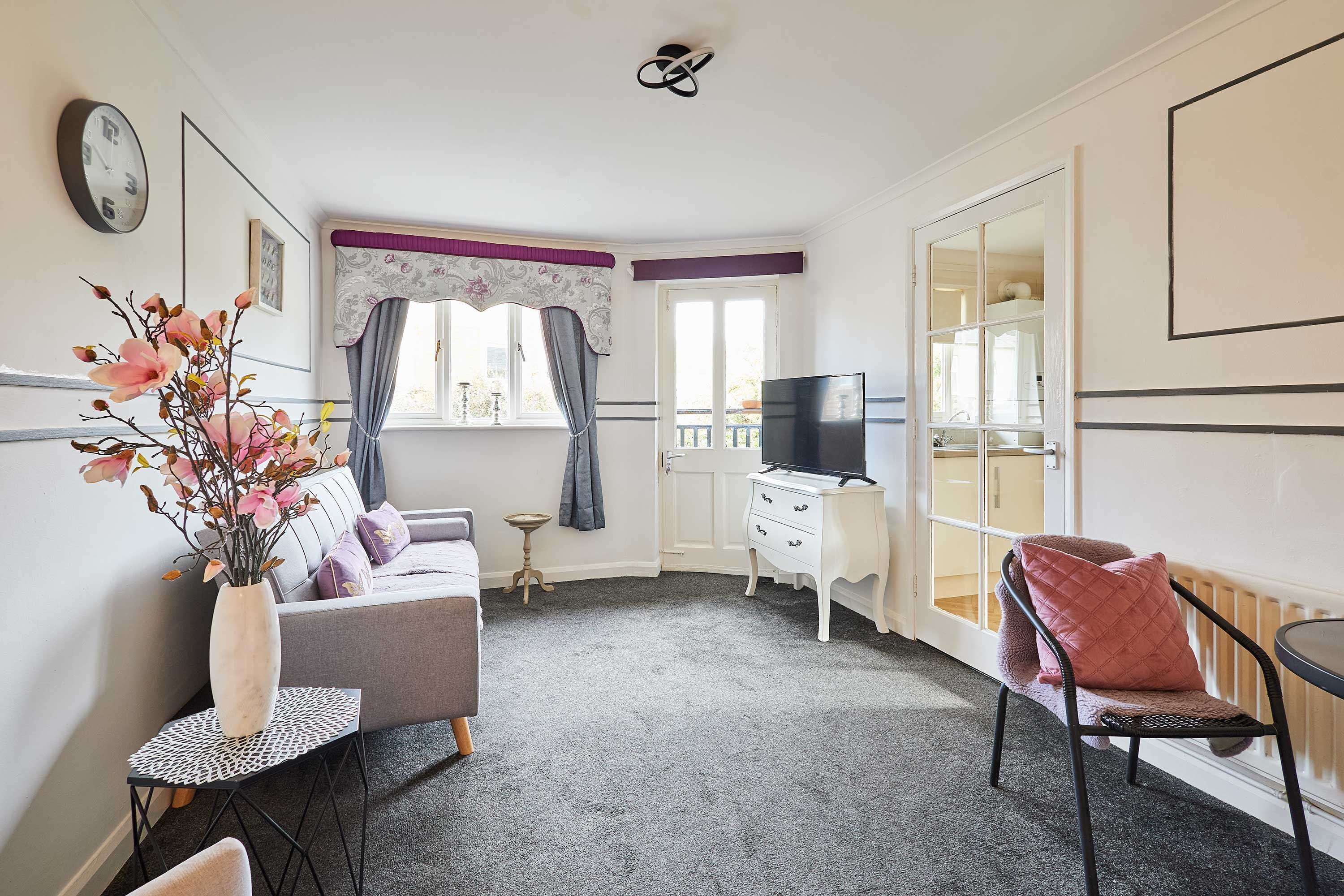 A compact living space with a sofa, a small table, a chair, a television, and a decorative plant.