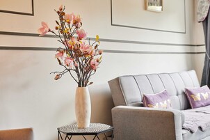 A room with a grey sofa, a white vase with pink flowers, and a small round table with a black base.