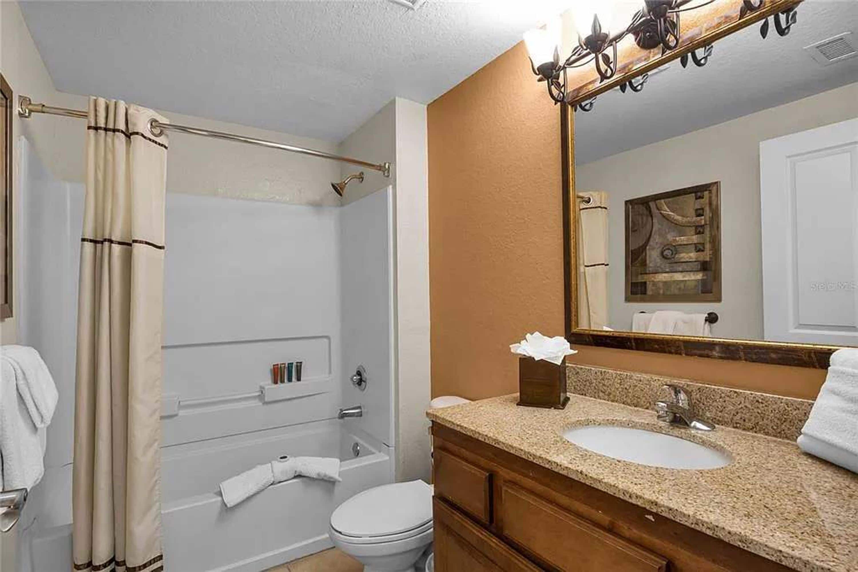 Ein Badezimmer mit Dusche, Toilette, Waschbecken und einem Spiegel mit Handtuchhalter.