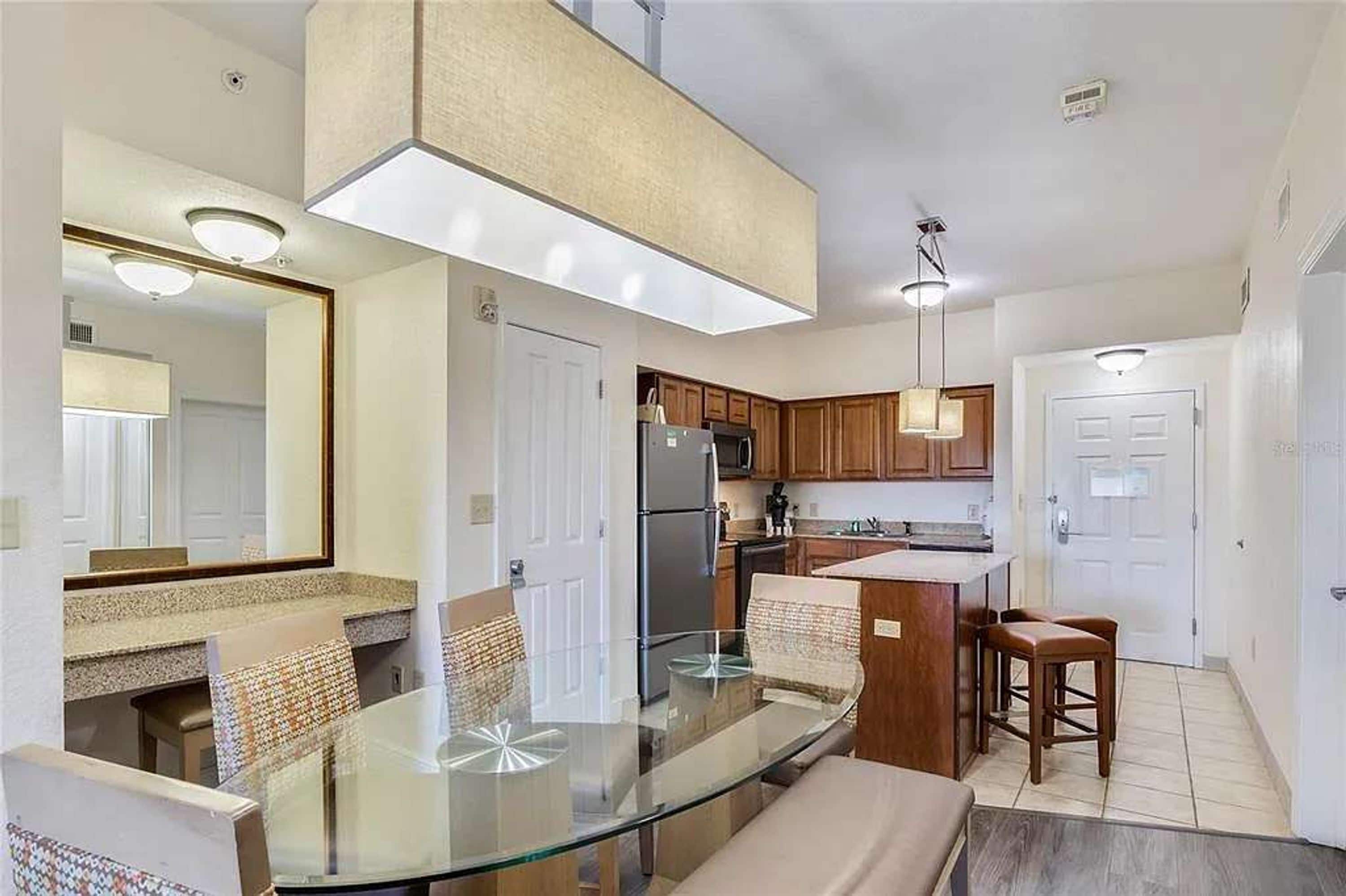 A modern kitchen with a glass dining table, wooden cabinets, and a built-in island.