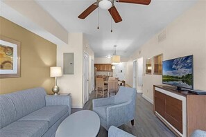A modern living room with a sofa, armchairs, a TV, and a ceiling fan. - Stay Near Disney 2BR Pools Arcade (Orlando)