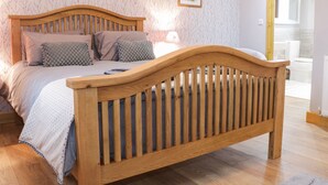 A bedroom with a wooden bed, patterned wallpaper, a framed picture on the wall, and a wooden door frame. - Gardener's Lodge (Nantwich)
