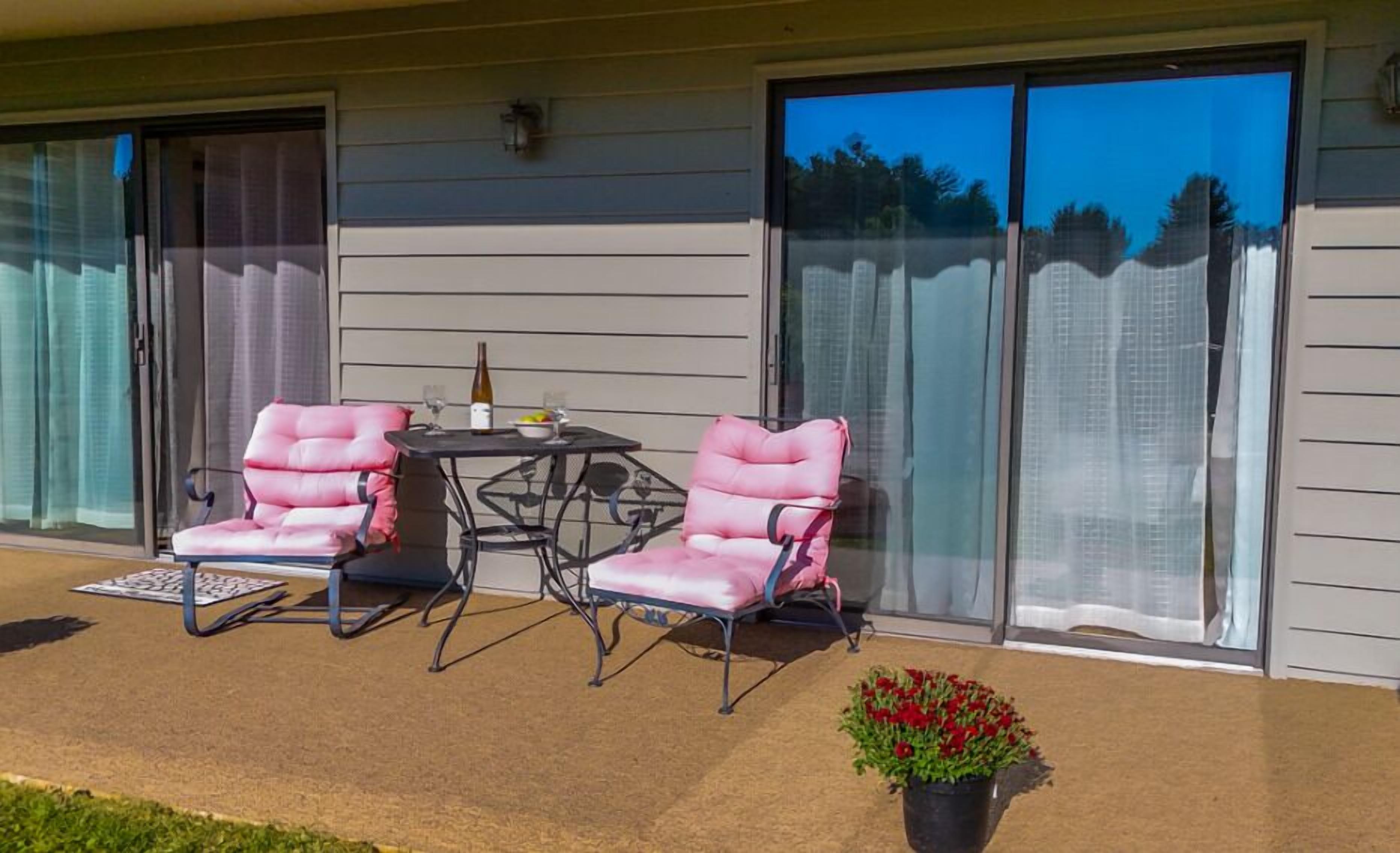 Une terrasse couverte avec deux chaises et une table, une bouteille de vin et une plante en pot.