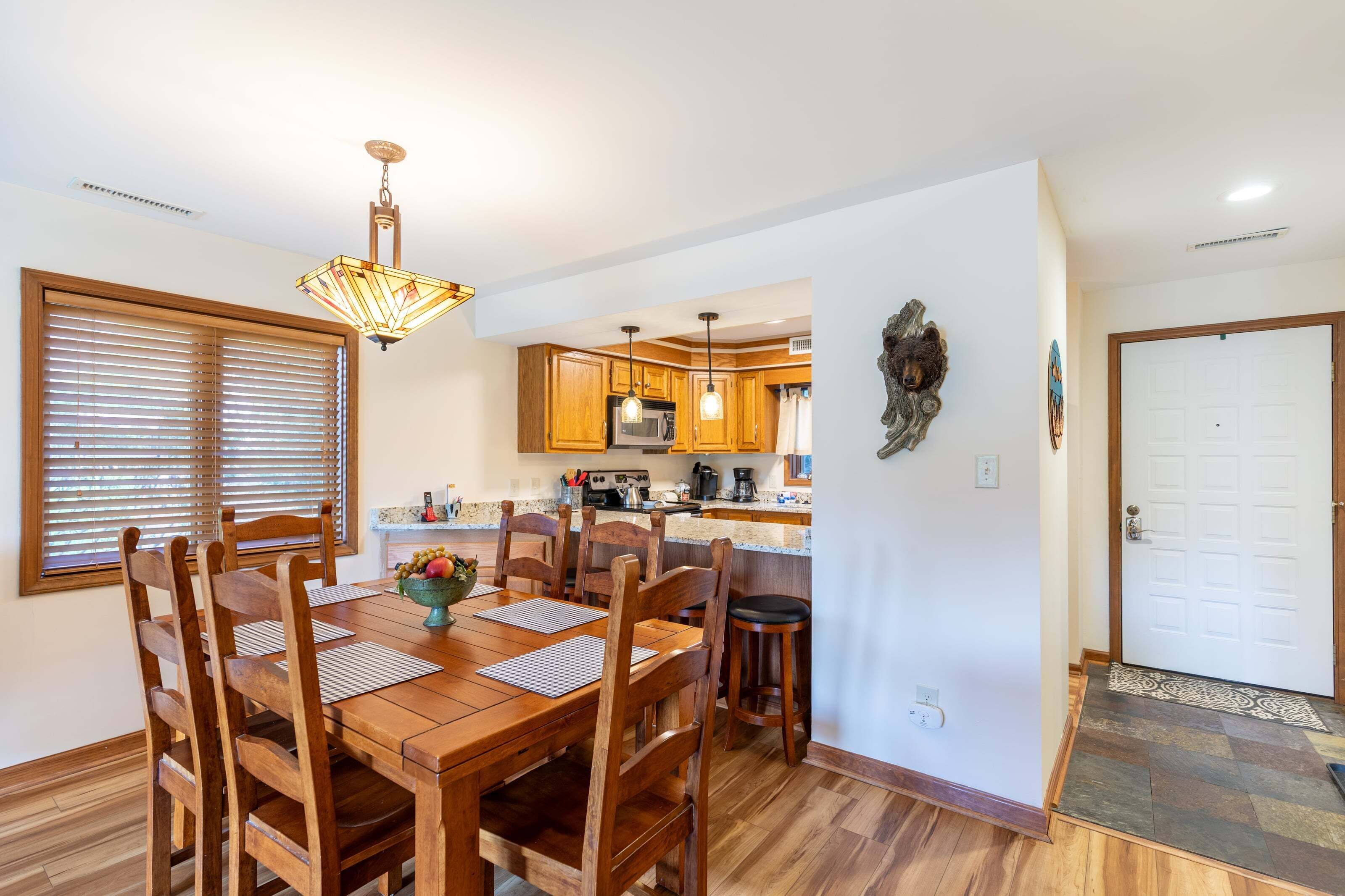 Un comedor con una mesa y sillas de madera, una araña y una cocina al fondo.