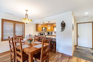 A dining area with a wooden table and chairs, a chandelier, and a kitchen in the background. - Cardinal 104 at Chetola: Updated 2br Ground Floor Condo with Wood Burning Fireplace (Blowing Rock)