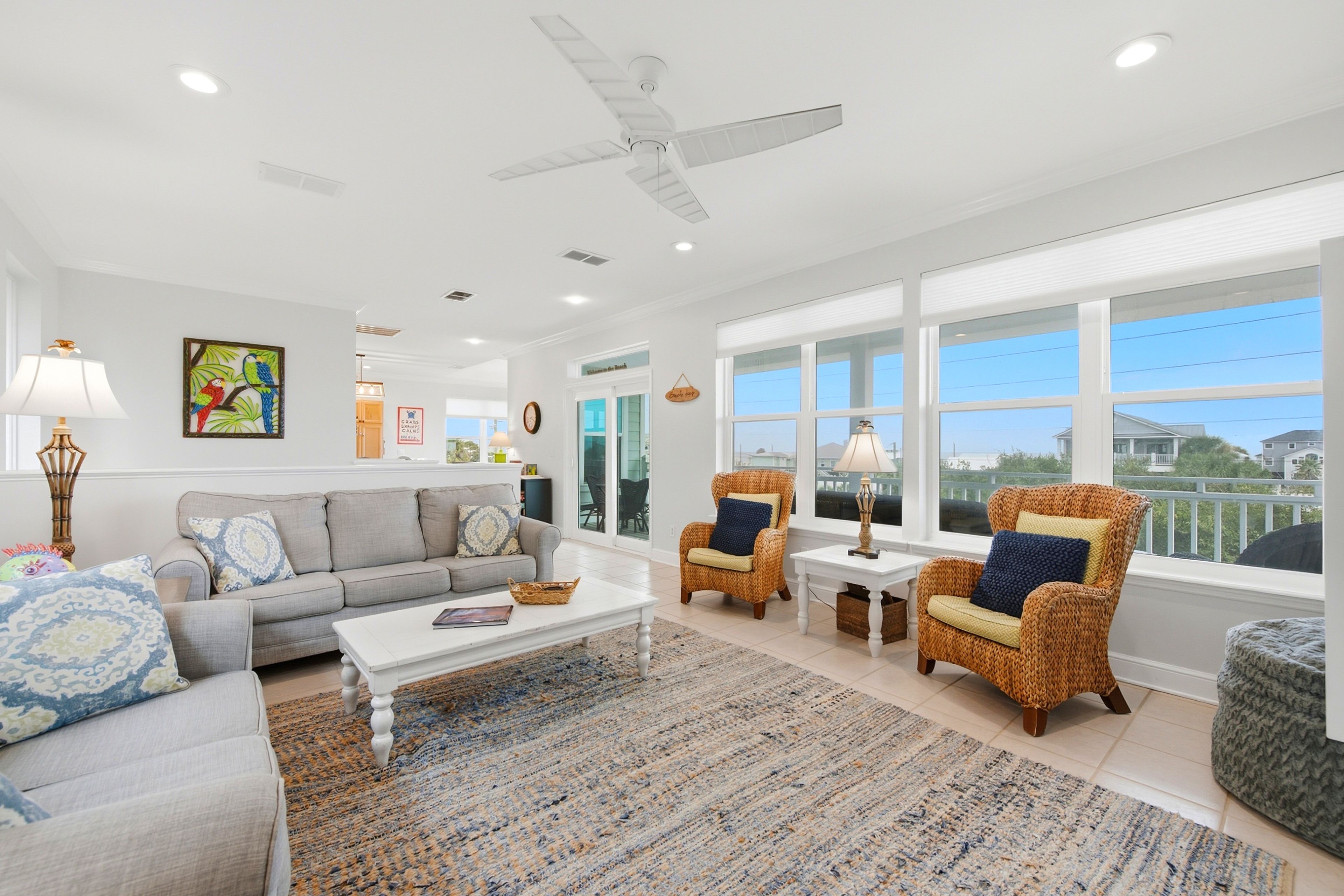 A spacious living room with a grey sofa, two wicker armchairs, a coffee table, and a ceiling fan.