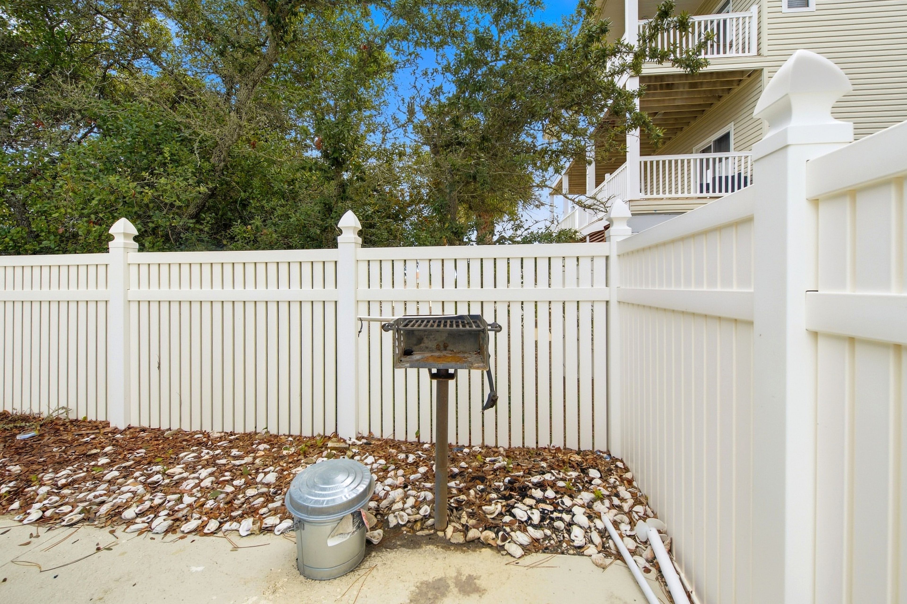 A fenced outdoor area with a grill and a trash can.